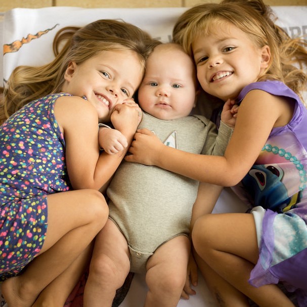Twin sisters embrace their infant brother.