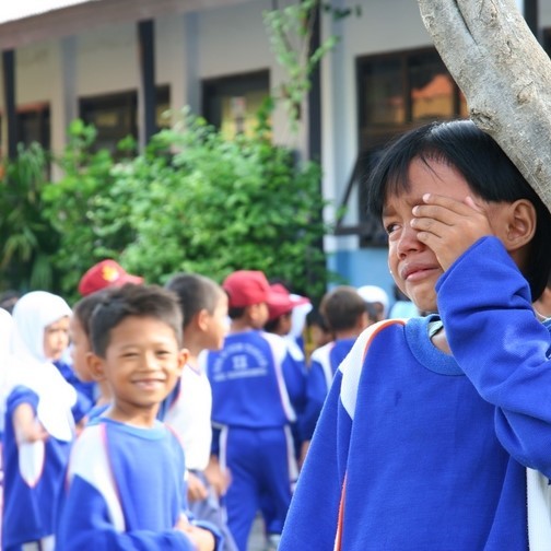A boy stands crying on the playground as another boy looks on smiling. A boy stands crying on the playground as another boy looks on smiling.