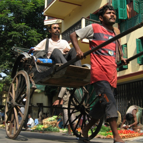A rickshaw driver pulls a passenger down a city street. A rickshaw driver pulls a passenger down a city street.